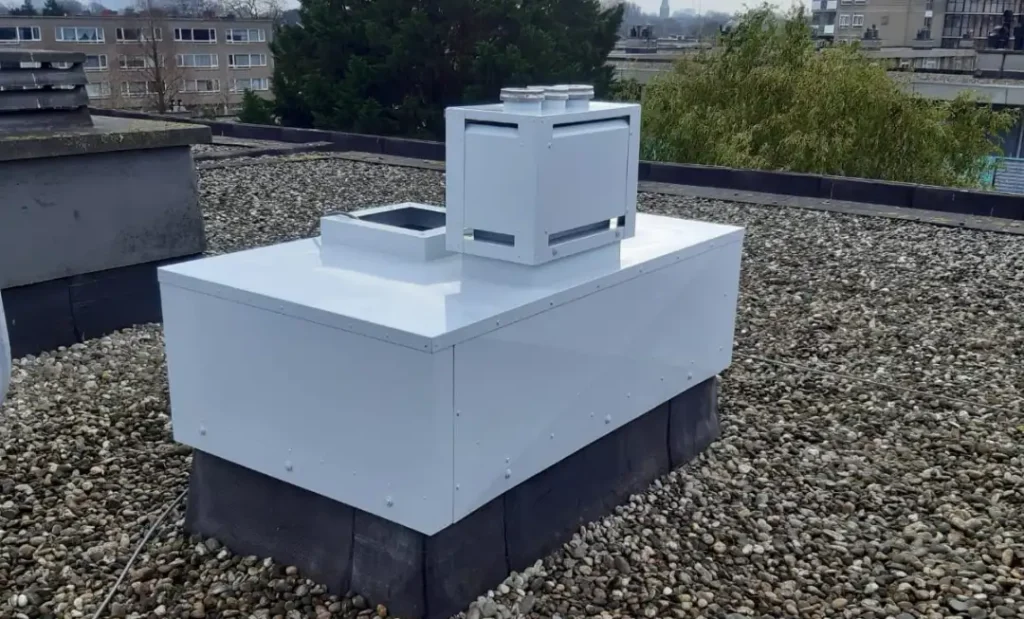 Wit plenum en ventilatie-unit voor rookgasafvoer op een plat dak, geïnstalleerd door HDA Haarlem in de provincie Noord-Holland.